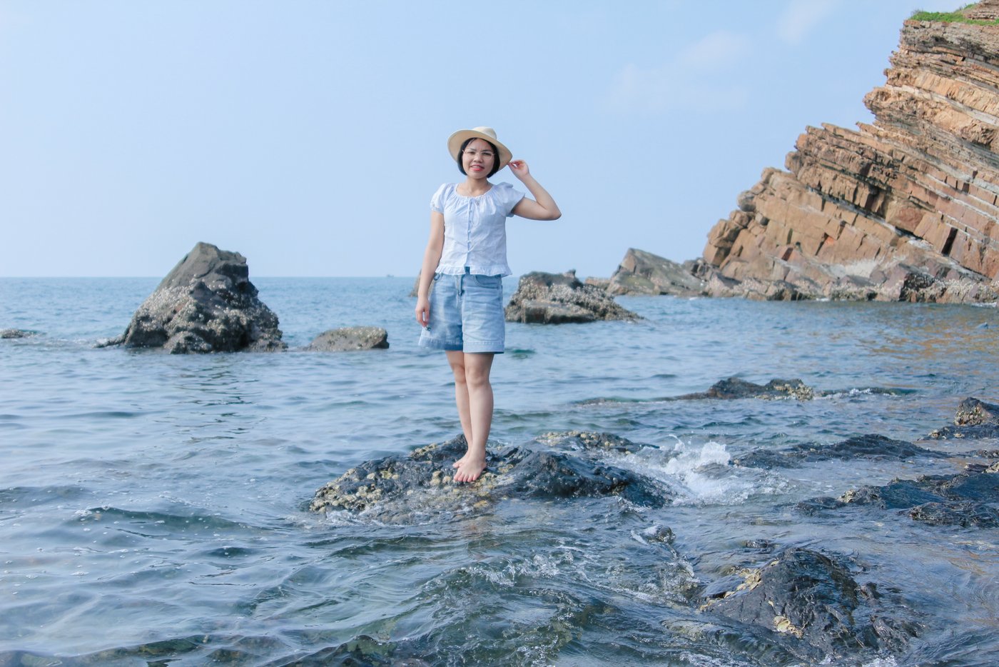 Home Woman in denim shorts standing on rocky coastline