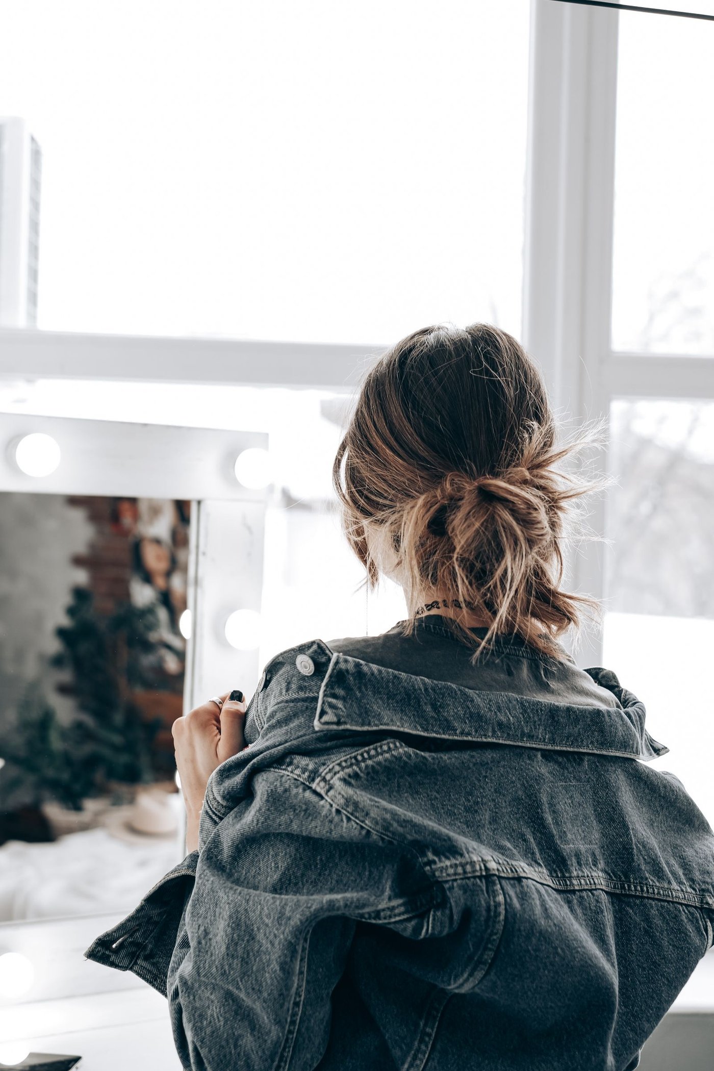 Back view of a woman in a denim jacket at a mirror