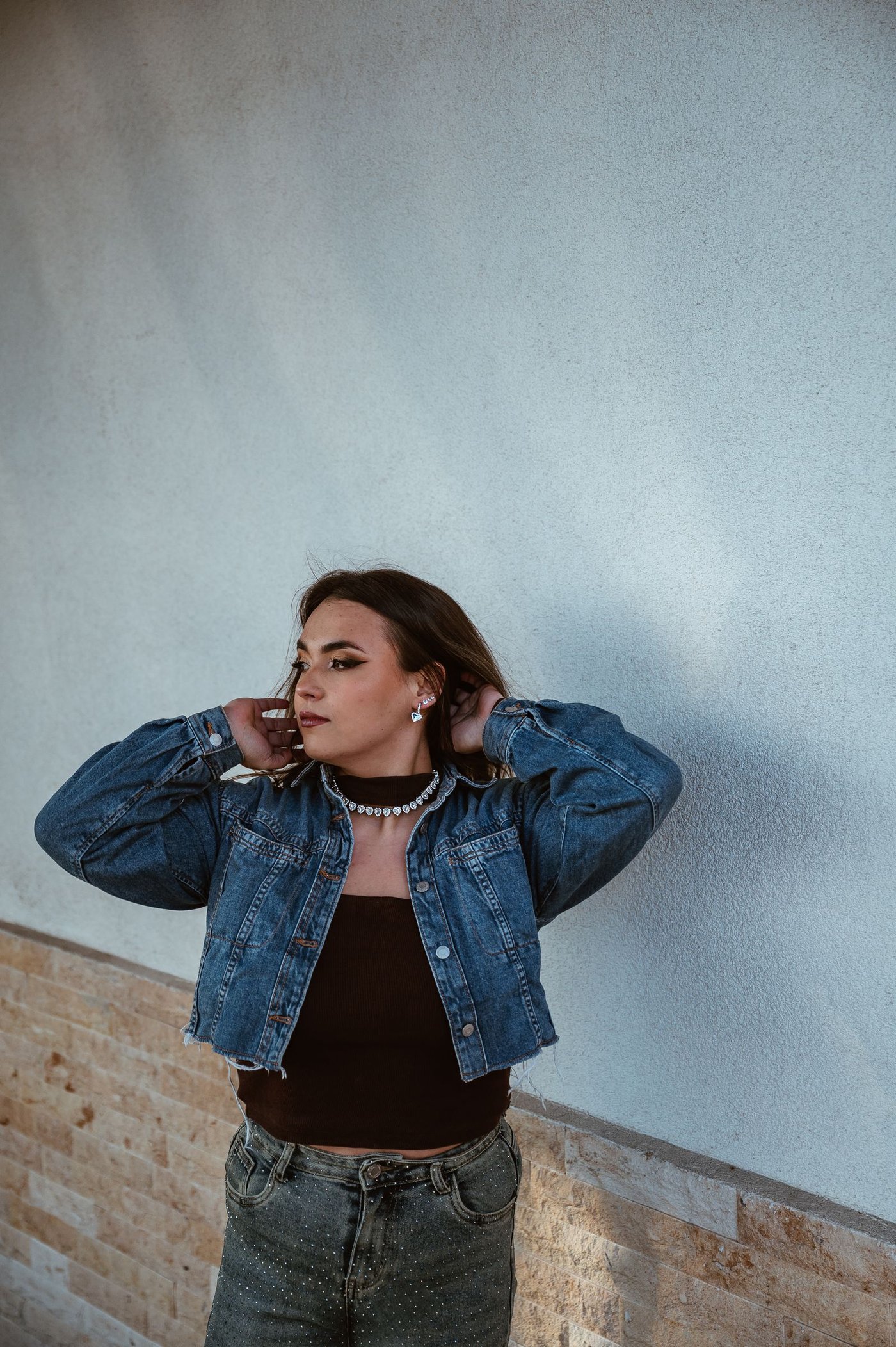 Woman in a denim jacket leaning against a plain wall